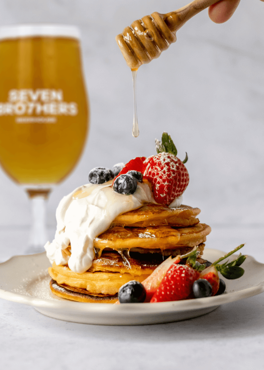 Pancakes with fruit and yoghurt, with a pint in the background.