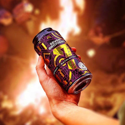 Hand holding a Seven Brothers Satin Stout can with a warm, blurred background.